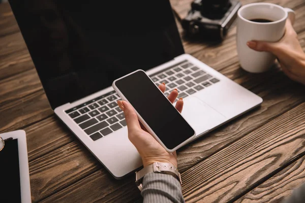 Vista recortada de freelancer femenino con teléfono inteligente, portátil, cámara de fotos retro y taza de café - foto de stock