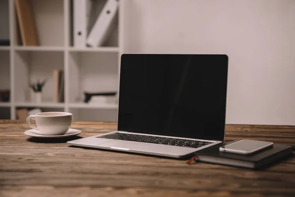 Laptop, smartphone e tazza di caffè su tavolo in legno in ufficio — Foto stock