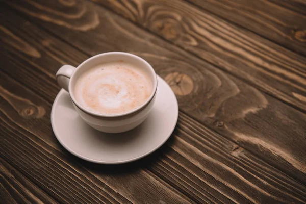 Soucoupe blanche et tasse avec cappuccino sur table en bois — Photo de stock