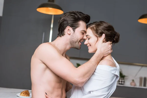 Взрослый мужчина и женщина улыбаются и обнимаются на кухне — стоковое фото