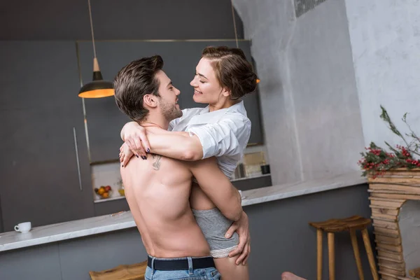 Улыбающаяся пара обнимается, стоя на кухне — стоковое фото