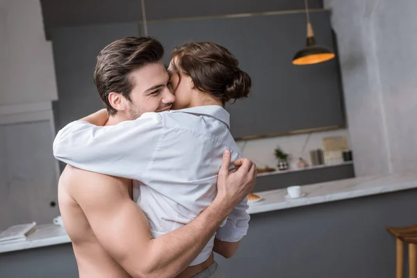 Sonriente hombre abrazando novia mientras de pie en la cocina — Stock Photo