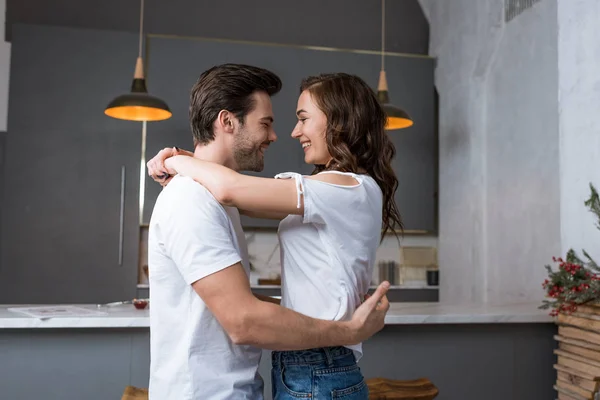 Sorrindo casal olhando um para o outro e abraçando na cozinha — Fotografia de Stock