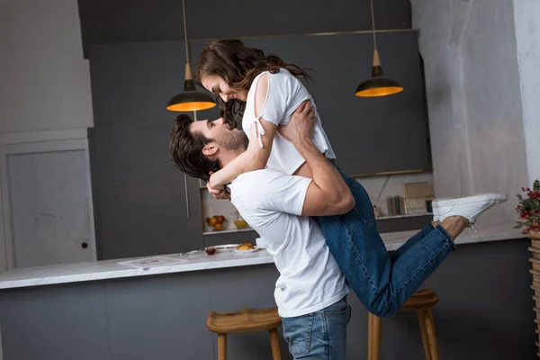 Hombre guapo sosteniendo en brazos atractiva novia en la cocina moderna - foto de stock