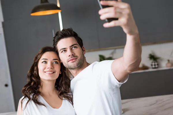 Hermosa novia y guapo novio tomando selfie en casa - foto de stock
