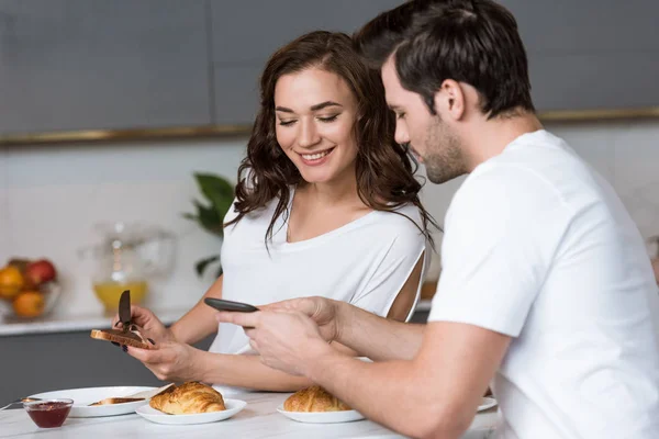 Woman looking at smartphone in hands of boyfriend in kitchen — Stock Photo