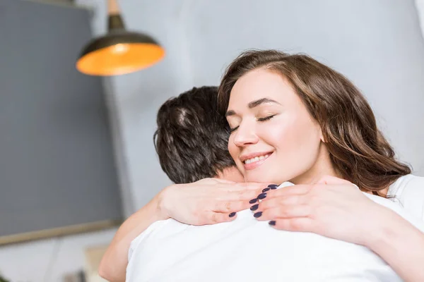 Feliz mujer atractiva abrazando novio y sonriendo en casa - foto de stock