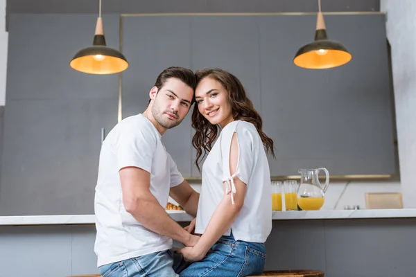 Casal feliz olhando para a câmera e de mãos dadas na cozinha — Fotografia de Stock