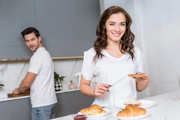 Focalizzazione selettiva della donna che tiene pane tostato e coltello vicino al fidanzato in cucina — Foto stock