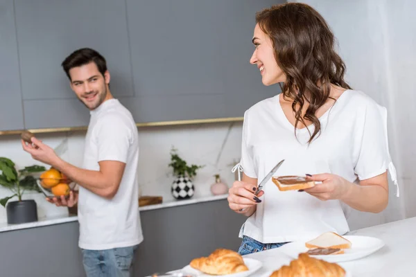Selective focus of woman smiling to boyfriend in kitchen — Stock Photo