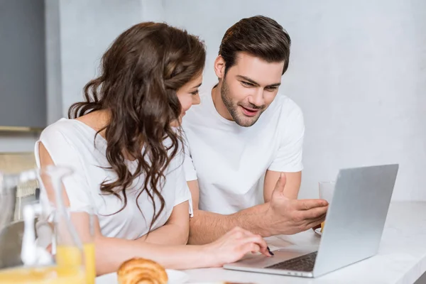 Atractiva mujer mirando novio usando portátil en la cocina - foto de stock