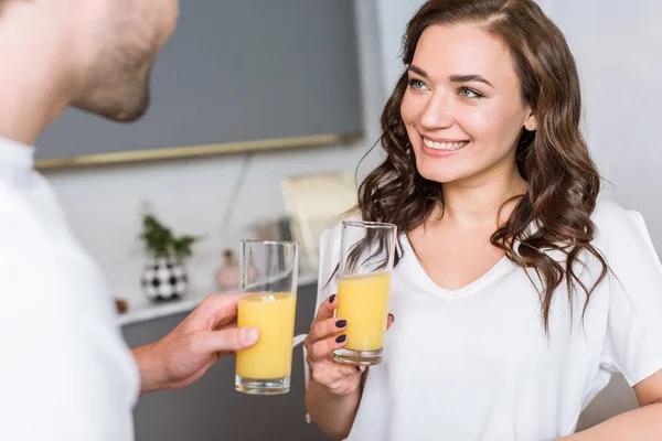 Messa a fuoco selettiva della donna attraente sorridente mentre tiene il vetro con succo d'arancia vicino al fidanzato — Foto stock