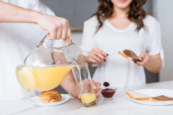 Selective focus of man pouring orange juice in glass near girlfriend in kitchen — Stock Photo