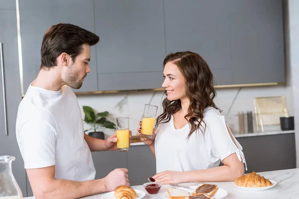 Namorada atraente olhando para namorado enquanto segurando vidro com suco de laranja na cozinha — Fotografia de Stock