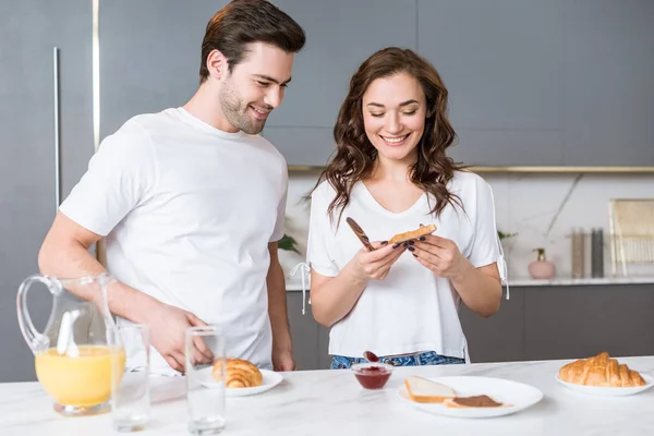 Casal alegre olhando para pão torrado e sorrindo na cozinha — Fotografia de Stock