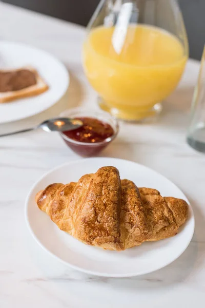 Foco seletivo de croissant saboroso com engarrafamento e suco de laranja no jarro no fundo — Fotografia de Stock