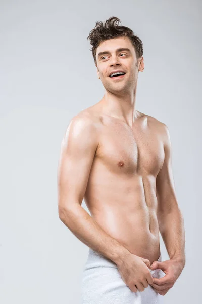 Handsome cheerful shirtless man posing in towel isolated on grey — Stock Photo