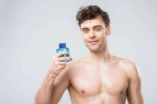 Мужчина без рубашки держит бутылку с одеколоном, изолированный на сером — стоковое фото