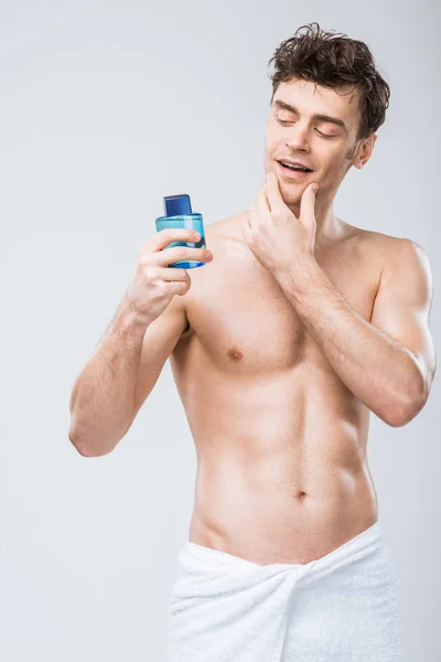 Handsome man looking at bottle with cologne, isolated on grey — Stock Photo