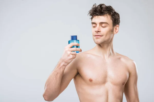 Hombre sin camisa guapo sosteniendo botella con colonia, aislado en gris - foto de stock