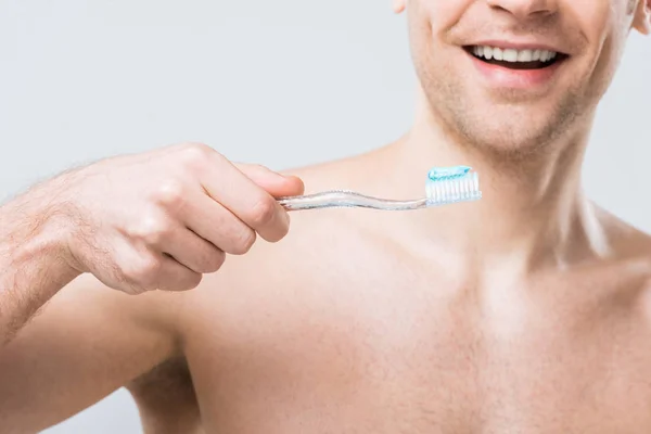Vista recortada del hombre sonriente sosteniendo el cepillo de dientes con pasta de dientes, aislado en gris - foto de stock