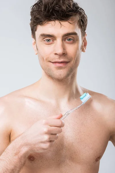 Joven sosteniendo cepillo de dientes con pasta de dientes, aislado en gris - foto de stock