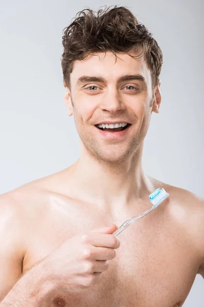 Homem sorridente segurando escova de dentes com pasta de dentes, isolado em cinza — Fotografia de Stock