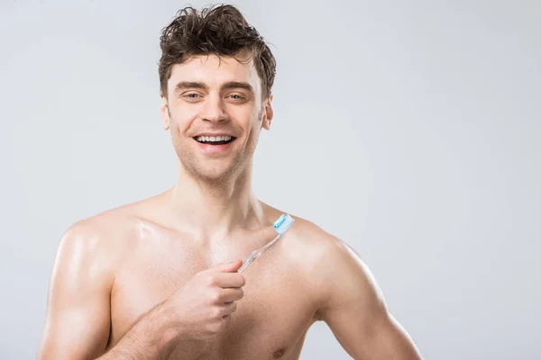 Bel homme souriant tenant une brosse à dents avec du dentifrice, isolé sur gris — Photo de stock