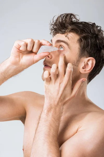 Young man dripping eye drops, isolated on grey — Stock Photo