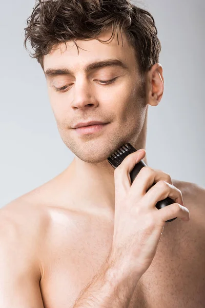 Молодий чоловік голиться з електричною бритвою ізольовано на сірому — стокове фото