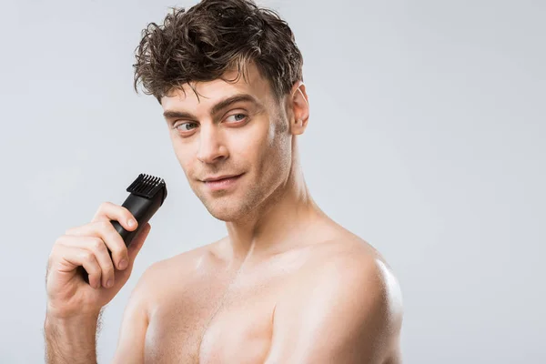 Hombre guapo sosteniendo máquina de afeitar eléctrica aislado en gris - foto de stock