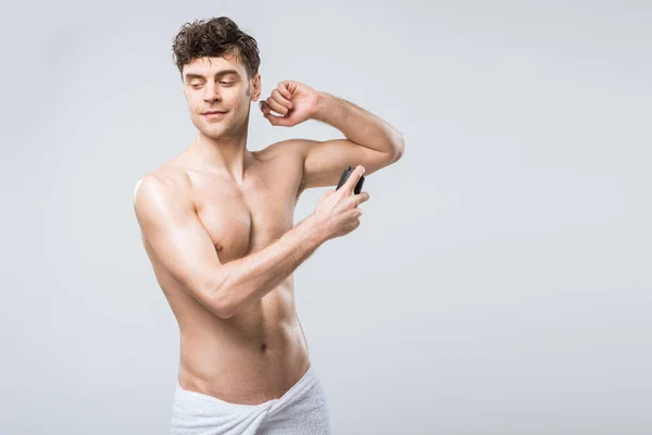 Hombre guapo sin camisa rociando desodorante, aislado en gris - foto de stock