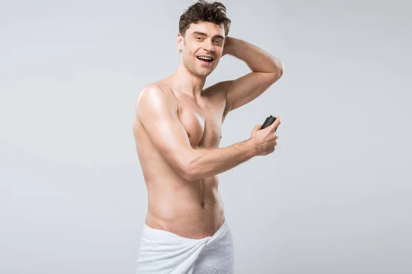 Красивый без рубашки возбужденный мужчина, распыляющий дезодорант, изолированный на сером — стоковое фото