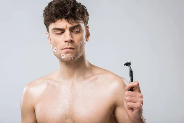 Confused man looking at razor after bad shaving, isolated on grey — Stock Photo