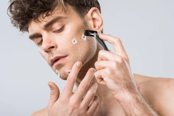 Hombre molesto con maquinilla de afeitar después de mal afeitado, aislado en gris - foto de stock