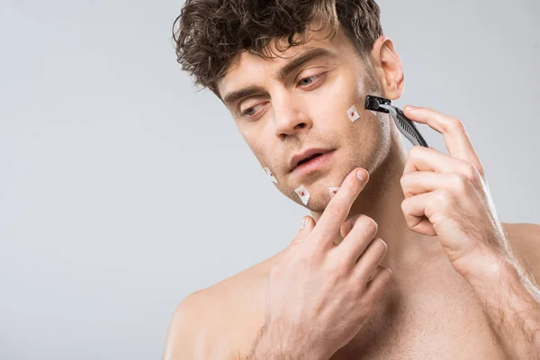 Hombre infeliz con maquinilla de afeitar después de mal afeitado, aislado en gris - foto de stock