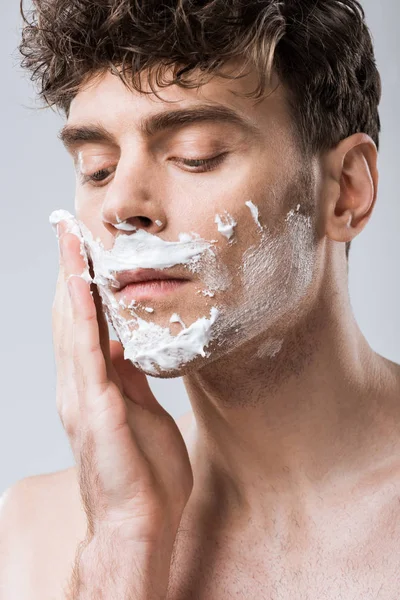 Close up de jovem aplicando espuma de barbear no rosto, isolado em cinza — Fotografia de Stock