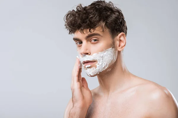 Красивий чоловік наносить піну для гоління на обличчя, ізольований на сірому — стокове фото