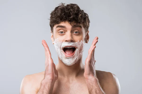 Eccitato uomo sorpreso urlando con schiuma da barba sul viso, isolato su grigio — Foto stock