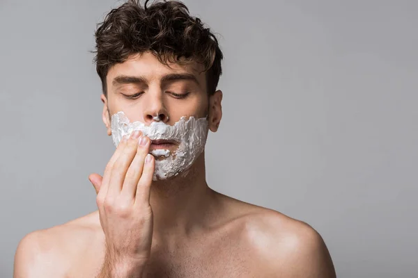 Homem bonito aplicando espuma de barbear no rosto, isolado em cinza — Fotografia de Stock