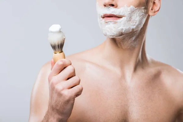Vista recortada del hombre aplicando espuma de afeitar con cepillo, aislado en gris - foto de stock