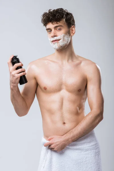 Handsome shirtless young man holding bottle with shaving foam, isolated on grey — Stock Photo