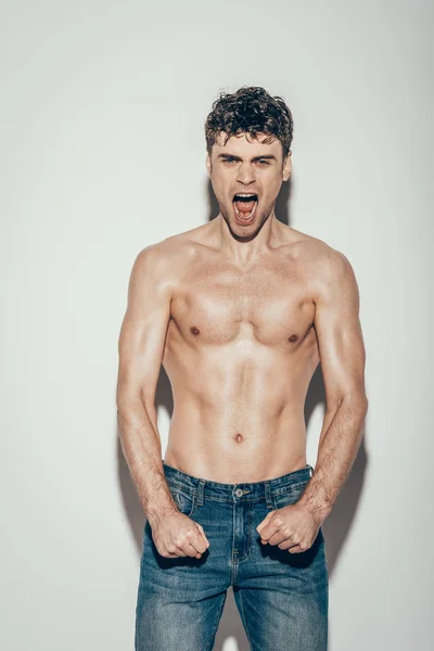 Sexy shirtless emotional man in jeans screaming and posing on grey — Stock Photo