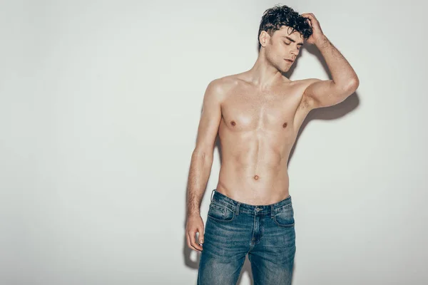 Sexy shirtless young man in jeans posing on grey — Stock Photo