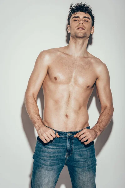 Handsome sexy shirtless man in jeans posing on grey — Stock Photo