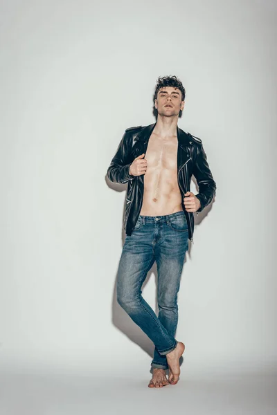 Bellissimo uomo sexy in posa in jeans e giacca di pelle nera su grigio — Foto stock