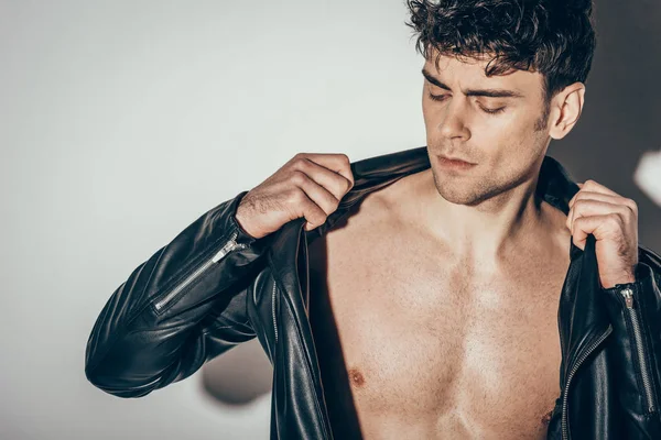 Handsome shirtless young man wearing black leather jacket on grey — Stock Photo