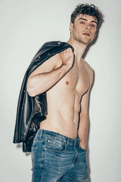 Sexy uomo senza camicia in posa con giacca di pelle nera su grigio — Foto stock