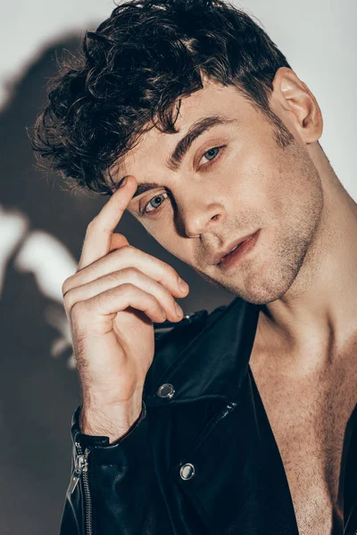 Портрет молодого сексуального мужчины, позирующего в черной кожаной куртке на сером — стоковое фото