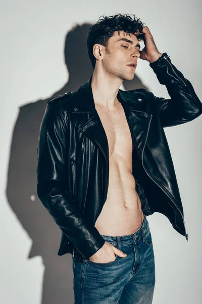 Schöner sexy Mann posiert in Jeans und schwarzer Lederjacke auf grau — Stockfoto